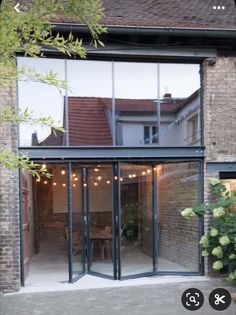 an open glass door leading to a patio with lights hanging from the ceiling and potted plants in front of it