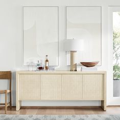 a white living room with two large paintings on the wall and a wooden sideboard