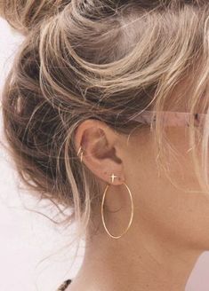 a woman with glasses wearing large gold hoop earrings and a black top knoted in to her hair