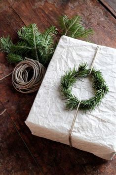 a wrapped present with a wreath on it next to some twine and pine branches