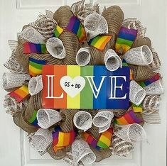 a wreath with the word love painted on it in front of a door decorated with colorful ribbons