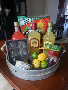 an assortment of drinks and condiments in a metal container on a table with a wooden surface