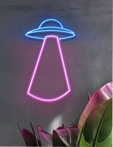 a neon sign with an alien hat on it's head in front of a plant