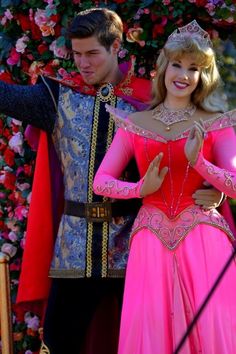 a man and woman dressed up as princesses standing next to each other in front of flowers