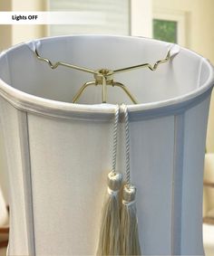 a white lamp shade with tassels hanging from it's sides and the light off