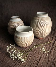 three white vases sitting next to each other on a brown surface with flowers in the foreground