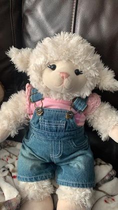 a white teddy bear wearing overalls and a pink shirt sitting on top of a couch