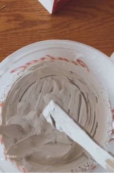 a white bowl filled with chocolate frosting on top of a wooden table next to a knife