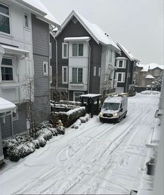 a van driving down a snow covered street in front of apartment buildings on a snowy day