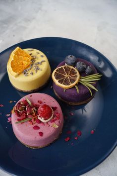 three desserts on a blue plate with orange slices and other food items around them