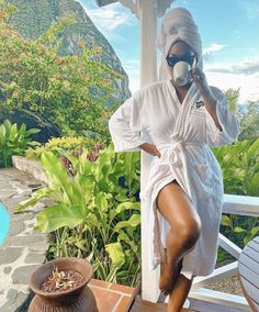 a woman in a bathrobe drinking from a cup on a porch next to a pool