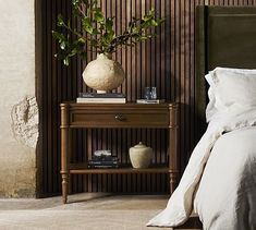 a bed sitting next to a night stand with a plant on it