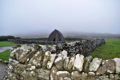 an old stone wall with a building in the background on a foggy, overcast day