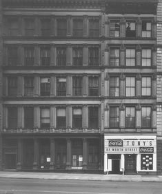 black and white photograph of an old building in new york city, with coca - cola advertisement on the front