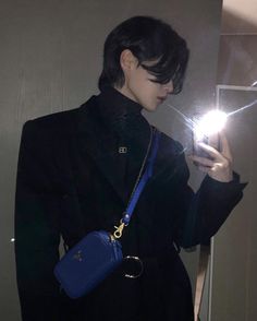 a woman holding a cell phone in her hand and wearing a black coat with a blue purse