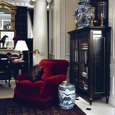 a red chair sitting next to a tall cabinet in a living room filled with furniture