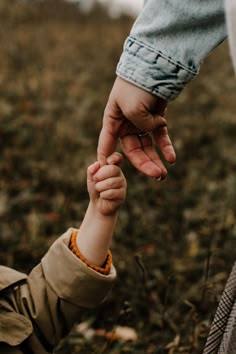 an adult holding the hand of a child's hand while standing in a field