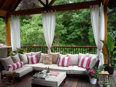 an outdoor living area with couches, tables and curtains on the outside decking