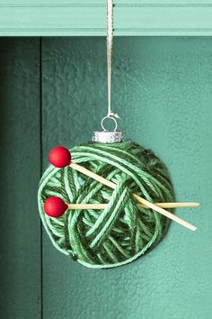 yarn ball ornament hanging on green door with knitting needles and balls of yarn