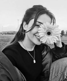 black and white photograph of a woman holding a flower in front of her face while sitting on the ground