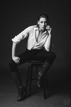 a black and white photo of a man sitting on a stool with his legs crossed