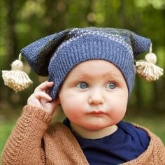 a baby wearing a blue hat with tassels on it's head and looking at the camera