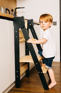 a little boy standing next to a black ladder