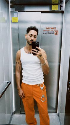 a man taking a selfie in an elevator with his cell phone and handcuffs around his ankles