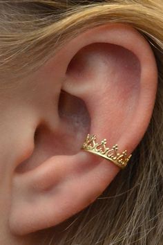 a close up of a person wearing a gold crown ear cuff on their left ear