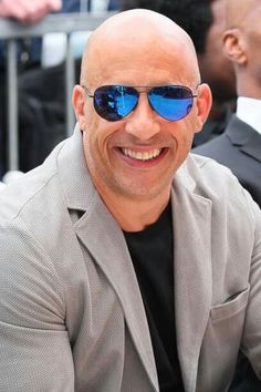 a bald man with blue sunglasses sitting in front of another man wearing a suit and tie