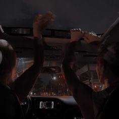 two people driving in the dark with their hands on the steering wheel and one person holding something up