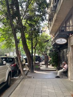 a man sitting on a chair in front of a tree lined street with parked cars