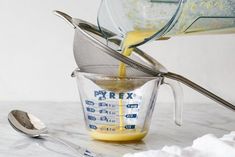 a measuring cup filled with yellow liquid next to a spoon