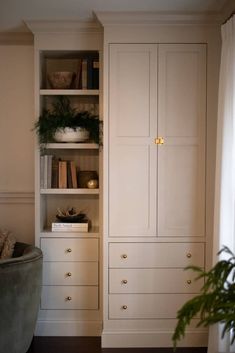 a tall white cabinet sitting next to a potted plant