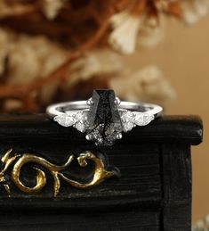 a black diamond ring sitting on top of a piece of wood next to a flower