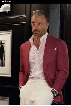 a man in a red jacket and white pants standing next to a black wall with pictures on it