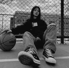 a woman sitting on the ground with a basketball in front of her and behind her is a chain link fence