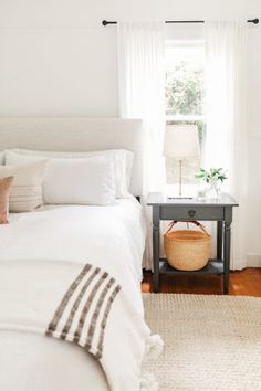 a bedroom with white linens and neutral colors in the bedding, along with a wicker basket