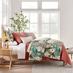 a bedroom with white walls and wooden flooring has a bed covered in an orange flowered comforter