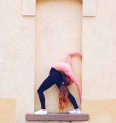 a woman leaning against a wall with her head on the ground and hands behind her back