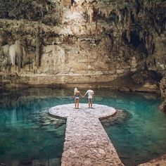 two people holding hands on a stone walkway in front of a pool with blue water