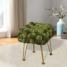 a green ottoman sitting on top of a white rug next to a vase with flowers