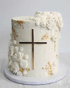 a white and gold wedding cake with a cross on the top, surrounded by flowers