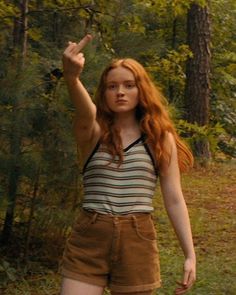 a young woman standing in the woods with her hand up