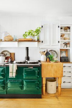 a green stove top oven sitting in a kitchen next to a wooden table and white cabinets