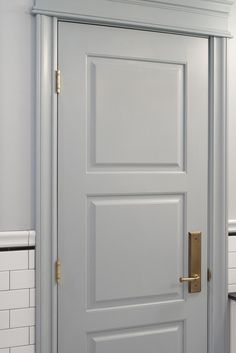 a white door with a gold handle in a bathroom area that has tile flooring and white walls