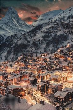 a town is lit up at night with mountains in the background and snow on the ground