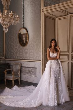 a woman in a white wedding dress standing next to a chair and chandelier