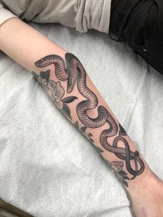 a person with a tattoo on their arm that has a snake and flowers on it