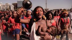 a group of people standing around each other holding a baby in their arms and one man with his face painted red